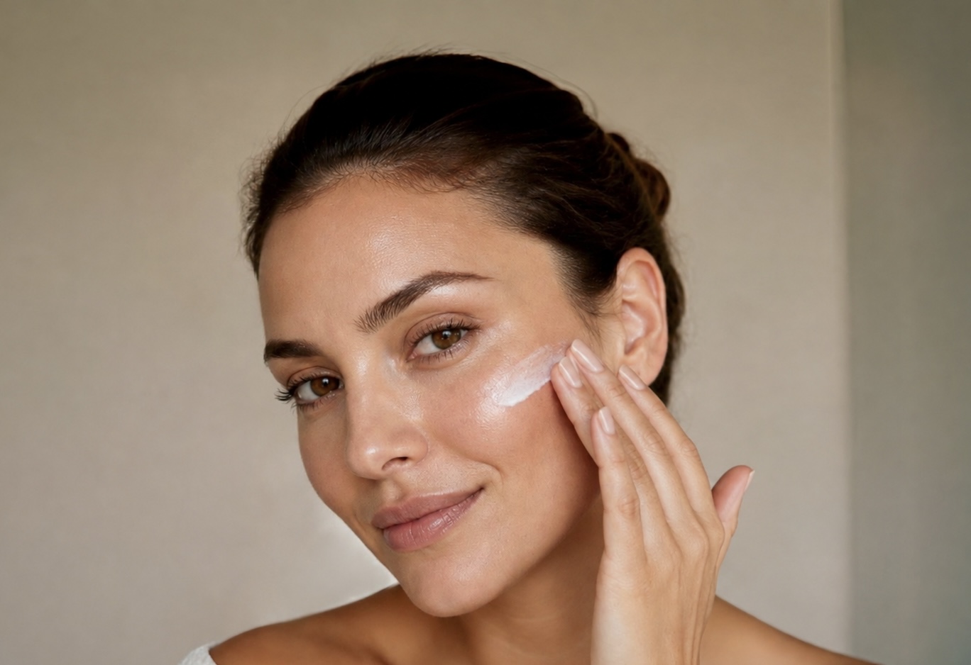 A woman applying moisturizer to her cheek as part of a preventative routine