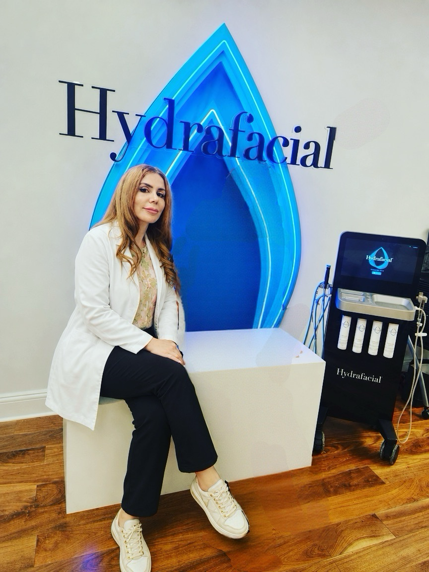 Mary Yegoryan, M.D., M.S., PA-C., seated beside the illuminated HydraFacial wall logo and the HydraFacial Syndeo machine at the Red Hook office